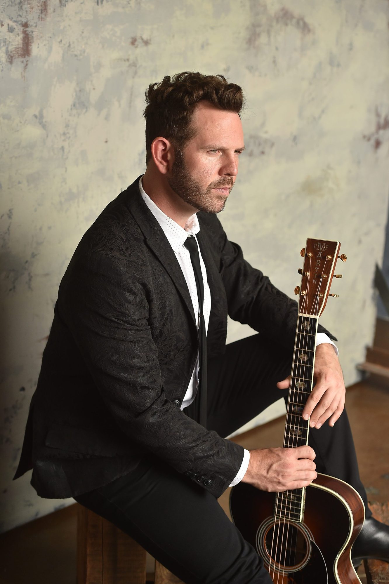 Matt Shockley in a black jacquard blazer holding his Martin acoustic guitar